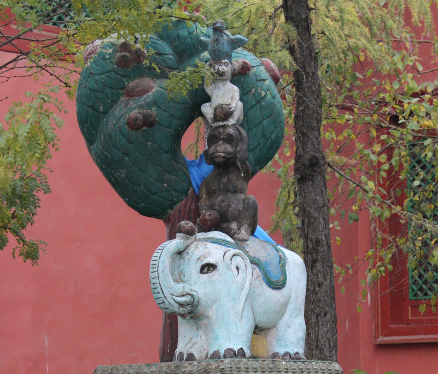 Die Statue von einem Elefanten, einem Affen, einen Hasen und einer Taube, die übereinander und unter einem Baum stehen