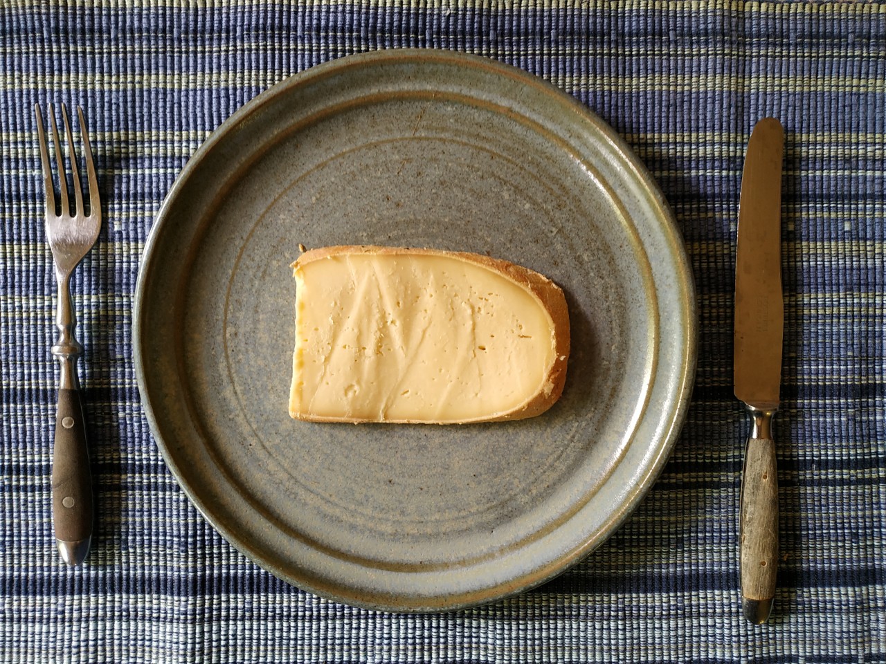 Eine Käsescheibe auf einem Teller mit Besteck