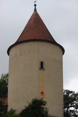 Turm mit kegelförmigem Dach. Ein blonder Zopgf hängt aus dem Turmfenster