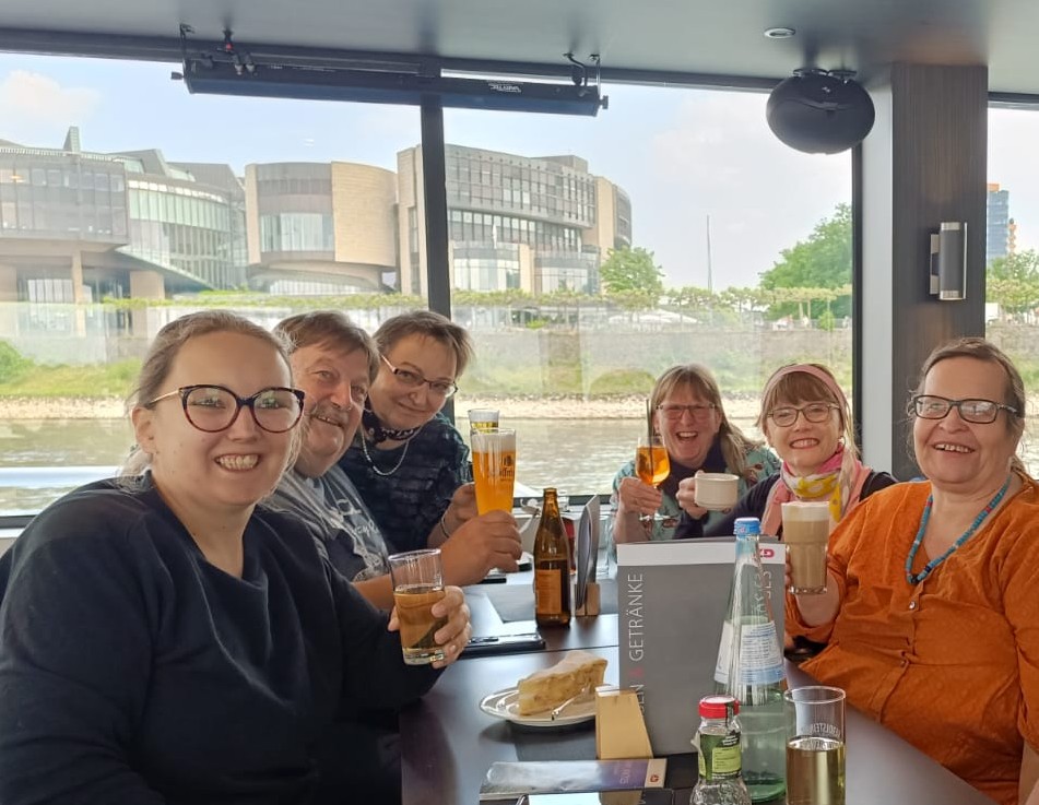 Die Mitglieder des Orgateam sitzen im Schiff am Tisch und feiern das gelungene Jahrestreffen