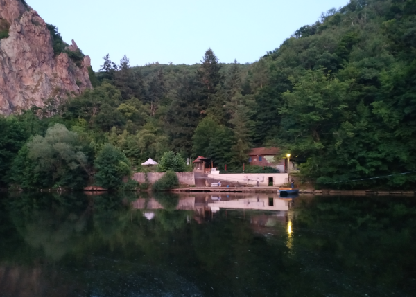 Am-anderen-Ufer-2 Im Fluss spiegeln sich ein dunkelgrüner Laubwald, ein Teil eines großen Felsens