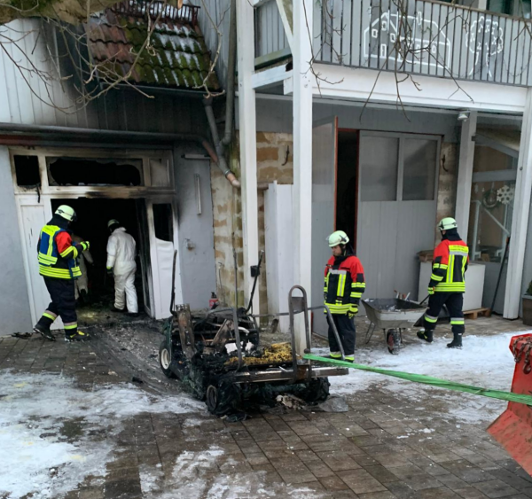 Feuerwehrleute untersuchen Brandschaden am Gebäude und am ausgebrannten elektrischen Golfcart.