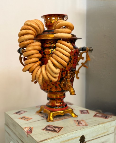 Verzierter Samowar, dekoriert mit Suschki (ringförmiges Gebäck), die an einer Schnur an ihm aufgehängt sind, auf einem Tisch mit Briefmarkenmotiven